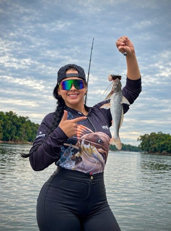 Pescadora com camiseta King mostrando o peixe na beira do rio