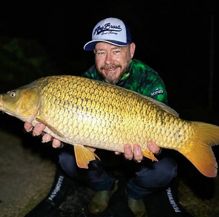 Pescador com camiseta King segurando uma carpa à noite
