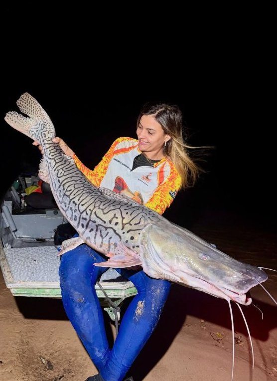 Pescadora com camiseta King segurando um peixe à noite
